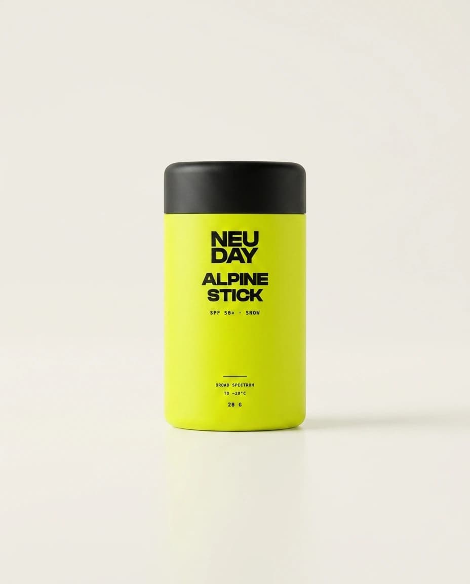 NEUDAY Alpine Stick SPF 50+ snow stick — a rugged volt-yellow push-up sunscreen stick with a matte-black base, on a warm bone studio background