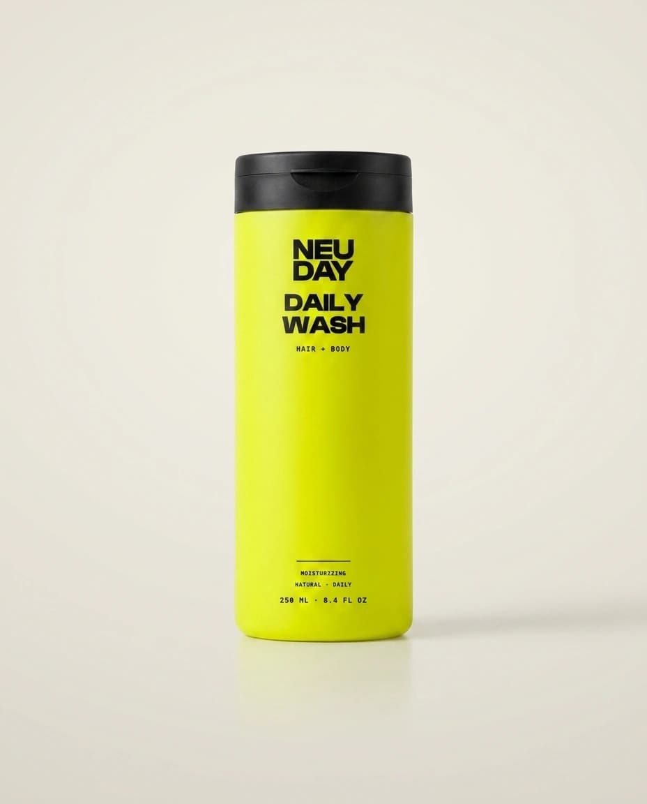 NEUDAY Daily Wash — a volt-yellow 250ml moisturizing hair & body wash bottle with a matte-black flip-top cap, on a warm bone studio background