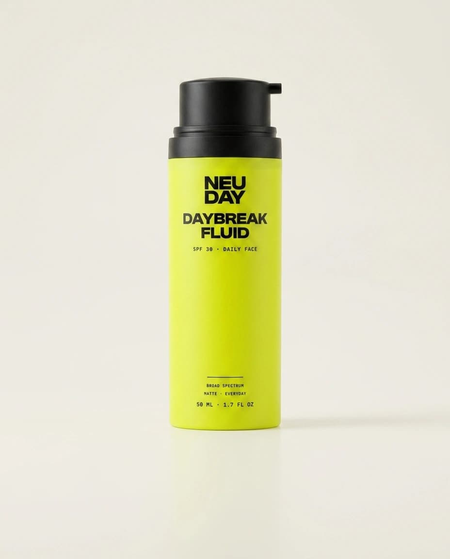 NEUDAY Daybreak Fluid SPF 30 — a volt-yellow daily face fluid bottle with a matte-black pump, on a warm bone studio background
