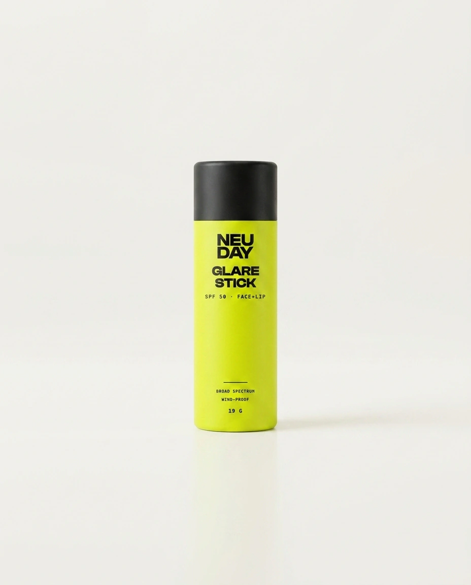 NEUDAY Glare Stick SPF 50 — a volt-yellow face and lip sunscreen stick with a matte-black base, on a warm bone studio background